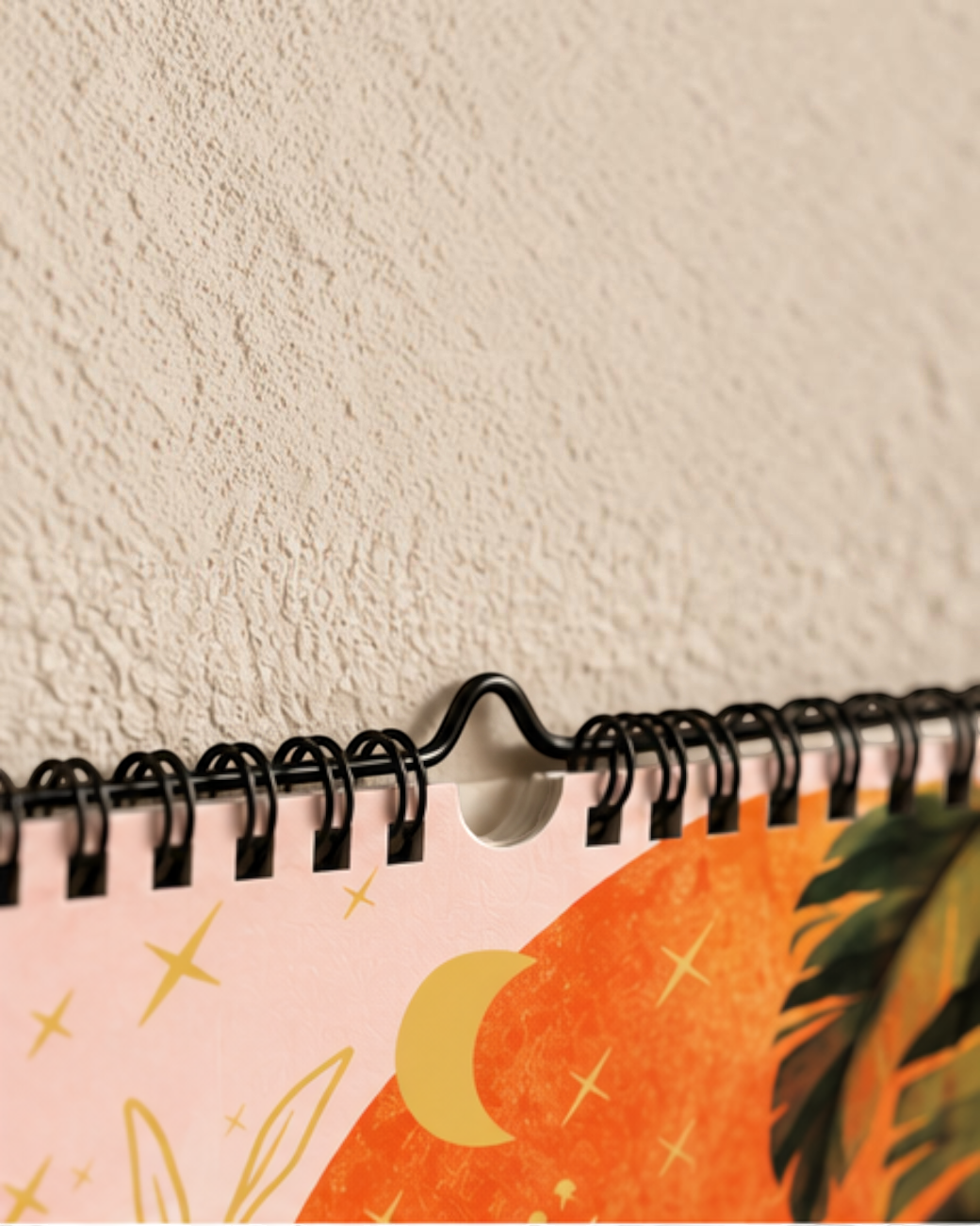 greenyogashop Yoga-Kalender 2027 mit Spiralbindung und illustriertem Mond- und Palmenmotiv an einer beigen Wand