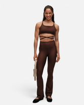 Model trägt dunkelbraune greenyogashop Flare High Waist Leggings mit ausgestelltem Bein und passendem Sport-BH