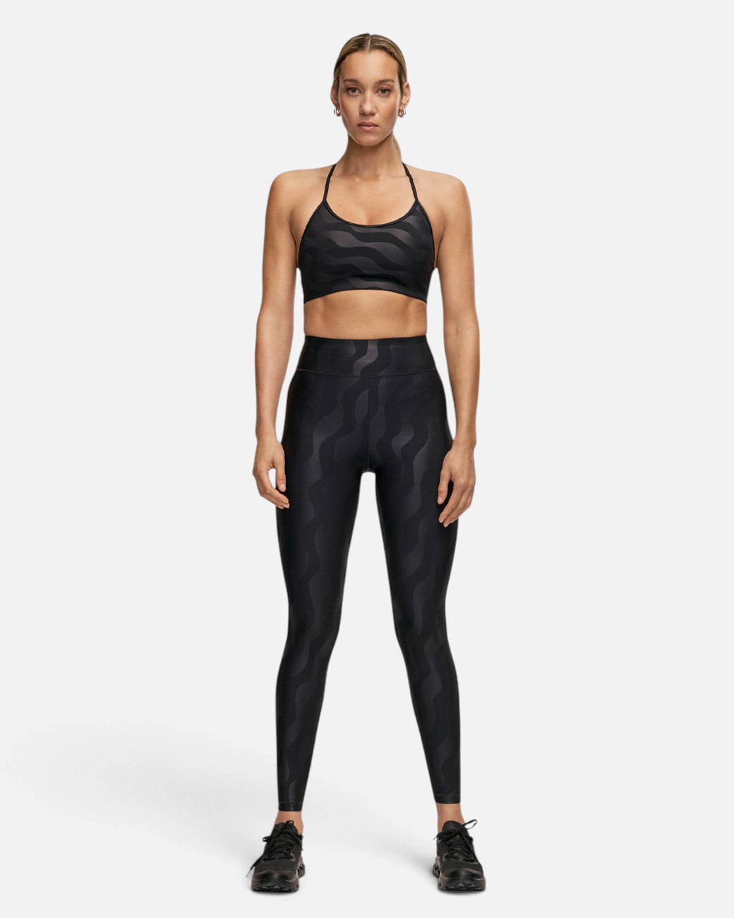 Model trägt greenyogashop High Waist Leggings in Schwarz mit grafischem Muster und passendem Sport-BH