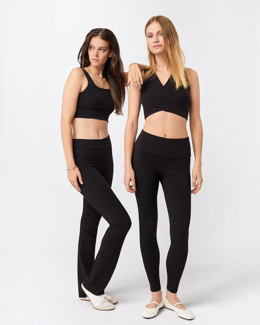 Zwei Models tragen schwarze greenyogashop Yogahosen mit Umschlagbund und passende schwarze Sport-Tops