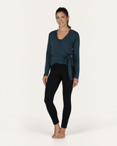 Model trägt grüne greenyogashop Aurora Wickeljacke aus Bambus-Mix mit Bindeband über einem Yoga-Top und Leggings