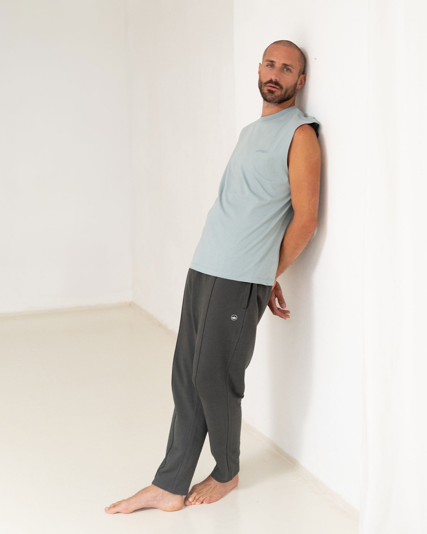 Stone Blue - Male Model steht an die Wand gelehnt in Yoga Tank